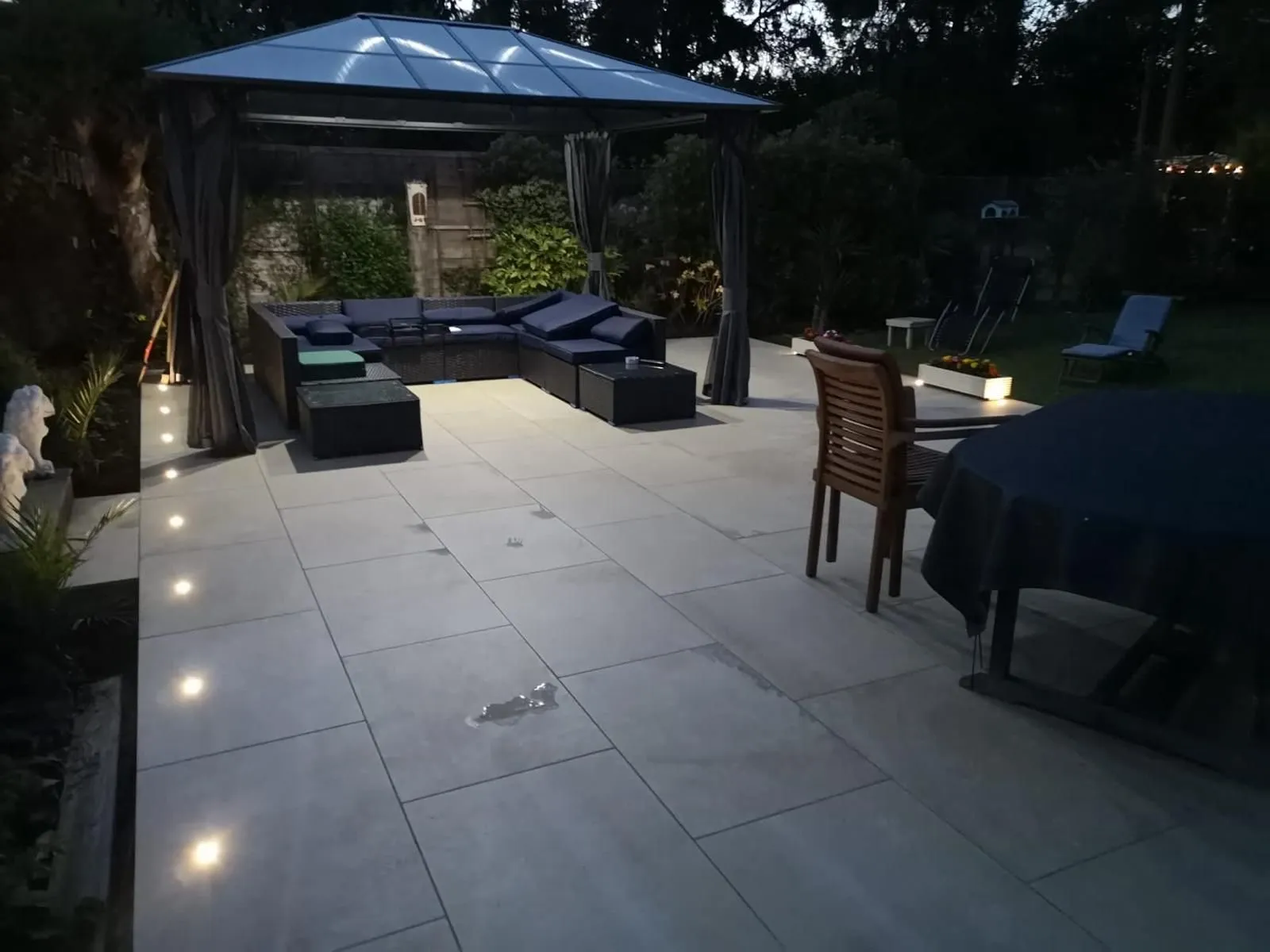 Grey porcelain patio at night with lit gazebo, recessed step lights and rattan seating